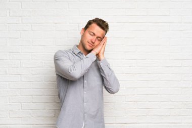 Beyaz tuğla duvar üzerinde sarışın adam aşkım ifade uyku jest yapma