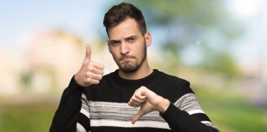 Yakışıklı adam iyi kötü işaret yapıyor. Açık havada Evet ya da değil arasında kararsız