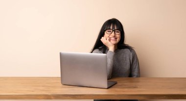 Dizüstü bilgisayarıyla çalışan genç bir kadın gözlüklü ve gülümseyen.