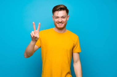 Mavi duvar üzerinde Redhead adam gülümseyerek ve zafer işareti gösteren