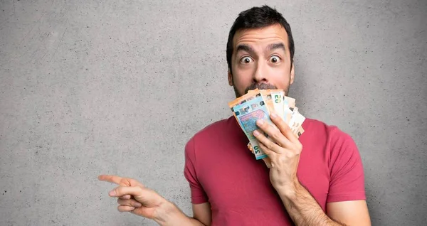 Adam dokulu duvar üzerinde sürpriz bir yüz ile yan parmak işaret çok para alarak