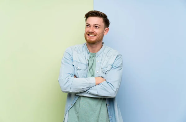 Redhead man over colorful background looking up while smiling