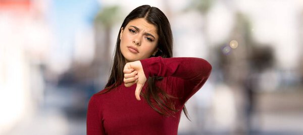Teenager girl with turtleneck showing thumb down with negative expression at outdoors