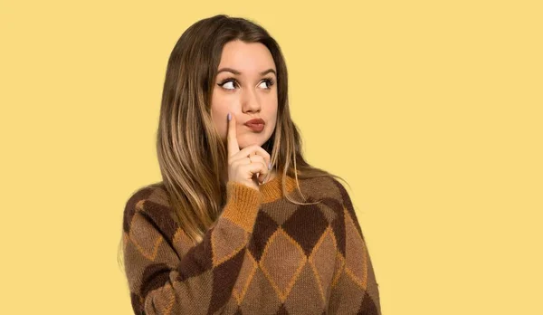 Teenager girl with brown sweater thinking over isolated yellow background