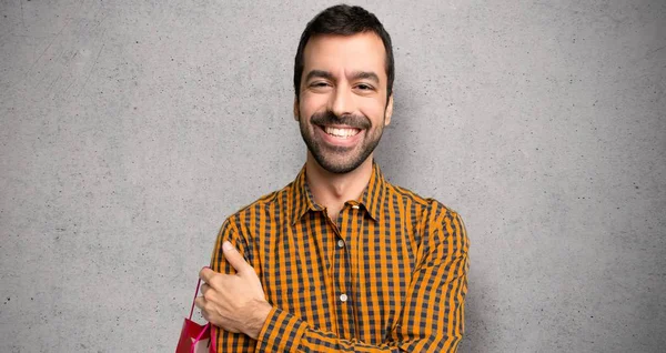 Mann Mit Einkaufstaschen Mit Glücklichem Gesichtsausdruck Über Strukturierter Wand — Stockfoto