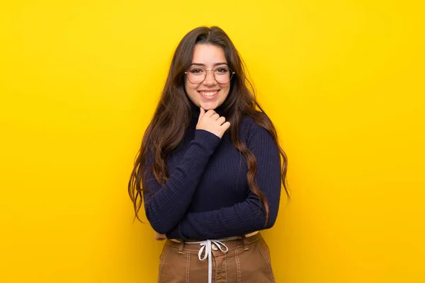Tiener Meisje Geïsoleerde Gele Muur Met Een Bril Glimlachend — Stockfoto