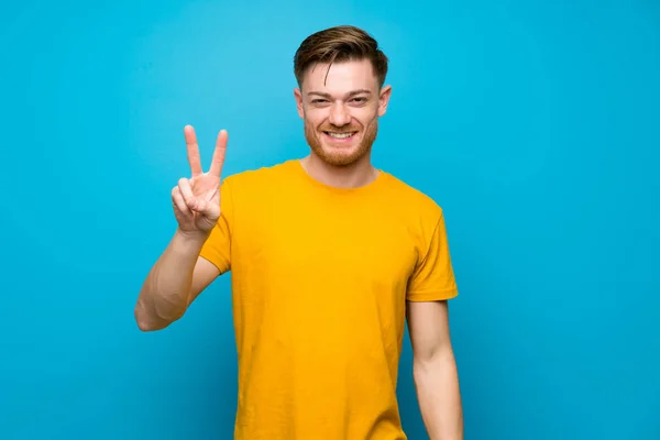 Pelirroja Hombre Sobre Pared Azul Sonriendo Mostrando Signo Victoria —  Fotos de Stock