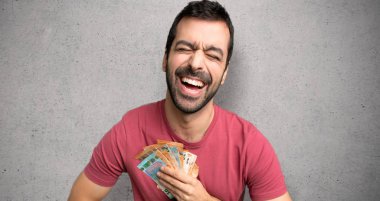 Adam bir sürü para alarak çok gülümseyen dokulu duvar üzerinde göğsüne eller koyarak