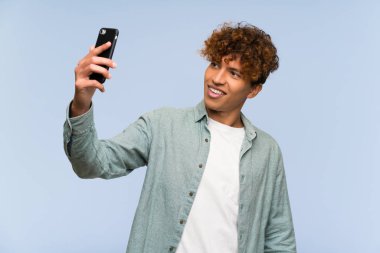 Genç Afro-Amerikan adam izole edilmiş mavi duvarın üstünde selfie çekiyor.