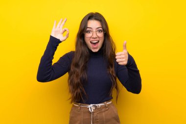 Genç kız üzerinde izole sarı duvar gösteren ok işareti ve Thumb yukarı jest