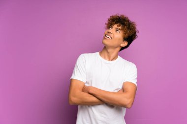 Genç Afro-Amerikalı adam, mor duvarın üzerinden gülümserken yukarı bakıyor.