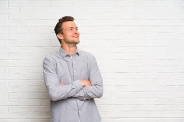 Gülümseyen iken beyaz tuğla duvar üzerinde sarışın adam bakıyor