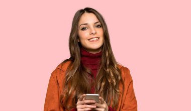 Ceket ile genç kadın izole pembe arka plan üzerinde cep ile bir mesaj gönderme