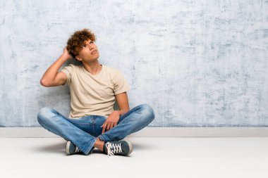 Genç Afro-Amerikan bir adam yerde oturuyor. Kafasını kaşırken şüpheleri var.