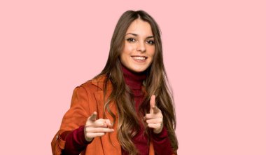 Ön işaret ve izole pembe arka plan üzerinde gülümseyen ceket ile genç kadın