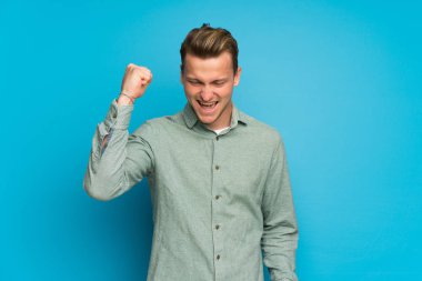 Sarışın adam bir zaferini kutluyor izole mavi duvarın üzerinden
