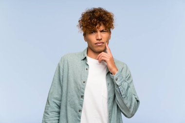 Genç Afro-Amerikan adam mavi duvarın üstünde. Önüne bakıyor.