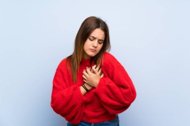 Kalp bir ağrı olan izole mavi duvar üzerinde genç kadın