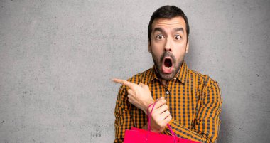 Alışveriş çantaları ile adam sürpriz ve dokulu duvar üzerinde yan işaret