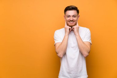 Kırmızı saçlı adam kahverengi duvar üzerinde mutlu ve hoş bir ifade ile gülümseyen