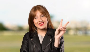 Genç Kızıl saçlı kadın gülümseyen ve açık havada zafer işareti gösteren