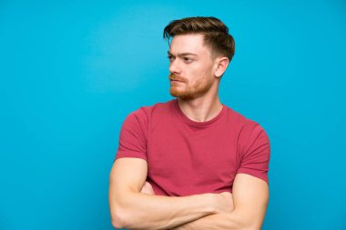 Izole mavi duvar ayakta ve yan görünümlü Redhead adam