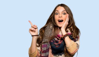 Genç hippi kadın yukarı işaret ve izole mavi arka plan üzerinde şaşırdı