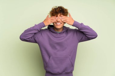 Genç Afro-Amerikan adam, izole edilmiş yeşil duvarın üzerinde gözleri elleriyle kaplayan.