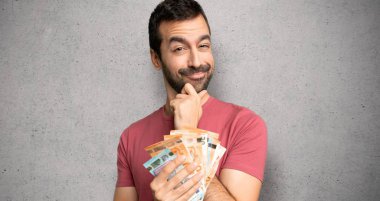 Adam gülümseyen ve dokulu duvar üzerinde emin yüzü ile ön bakarak para çok alarak