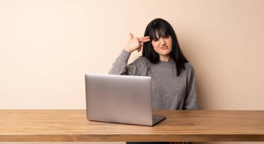 Dizüstü bilgisayarıyla çalışan genç bir kadın intihar jesti yapıyor.