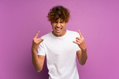 Genç Afro-Amerikalı adam, mor duvarın üstünde taş jestler yapıyor.