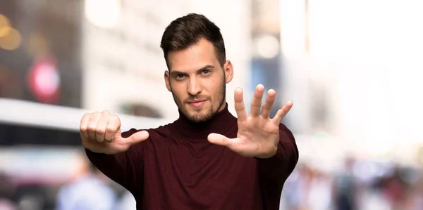 Man with turtleneck sweater counting six with fingers in the city