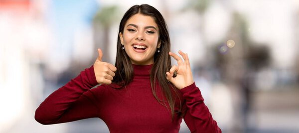Teenager girl with turtleneck showing ok sign with and giving a thumb up gesture at outdoors