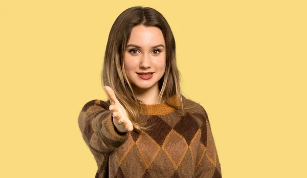 茶色のセーターを持つティーンエイジャーの少女は 孤立した黄色の背景の上に良い取引を閉じるために手を振る — ストック写真