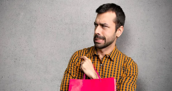 Alışveriş çantaları ile adam biraz gergin ve dokulu duvar üzerinde diş basarak korkuyor