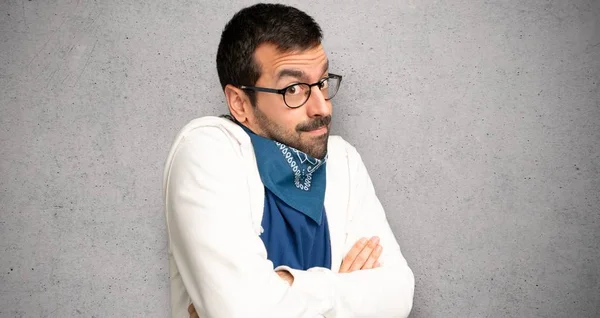 Handsome man with glasses making doubts gesture while lifting the shoulders over textured wall