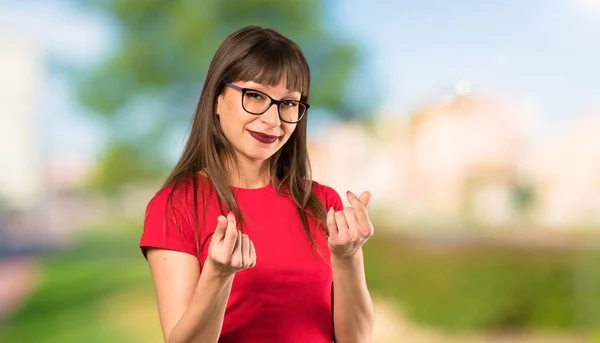 Woman with glasses making money gesture at outdoors