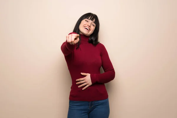 Young woman with red turtleneck pointing with finger at someone and laughing a lot