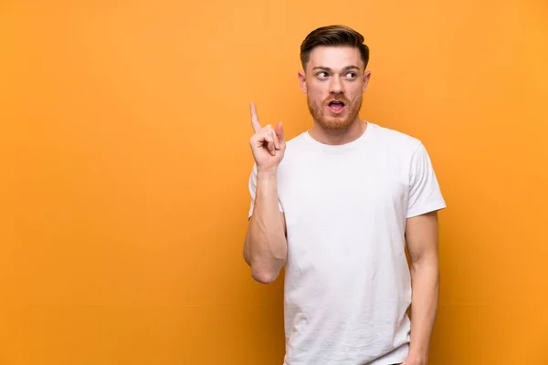 Redhead man over brown wall thinking an idea pointing the finger up