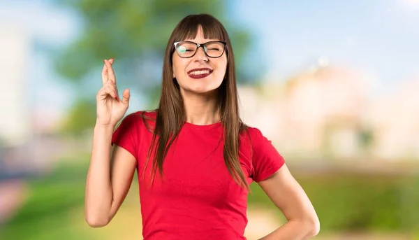 Woman with glasses with fingers crossing and wishing the best at outdoors