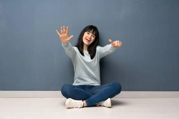 Woman sitting on the floor counting six with fingers