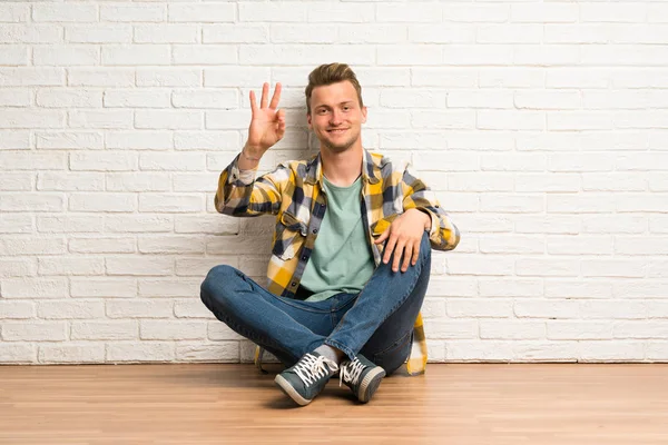 Blond Man Sitter Golvet Lycklig Och Räkna Tre Med Fingrarna — Stockfoto