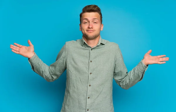 Blonde Man Geïsoleerde Blauwe Muur Met Twijfels Terwijl Het Verhogen — Stockfoto