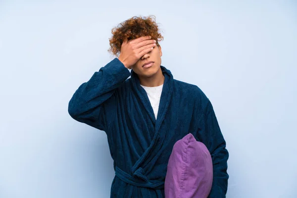 Young african american man in pajamas covering eyes by hands