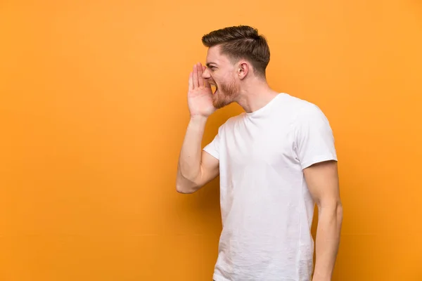 Redhead man over brown wall shouting with mouth wide open to the lateral