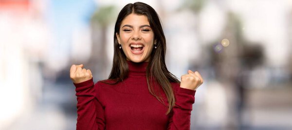 Teenager girl with turtleneck celebrating a victory in winner position at outdoors