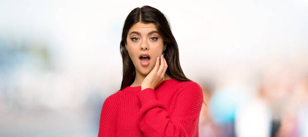 Teenager girl with red sweater surprised and shocked while looking right at outdoors