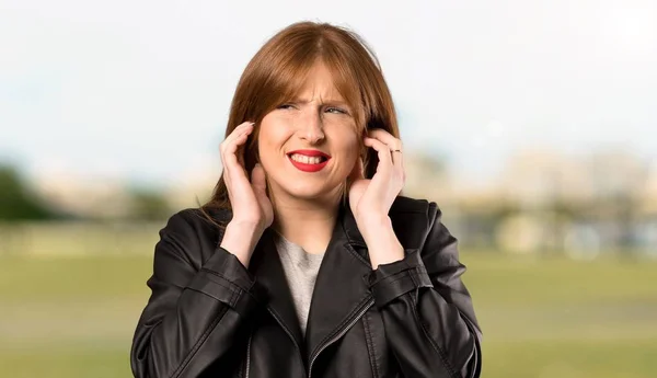 Young redhead woman frustrated and covering ears with hands at outdoors