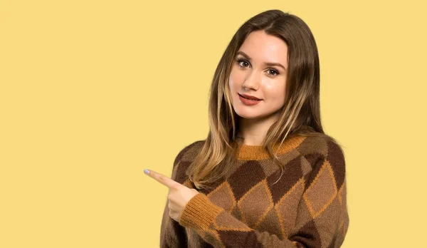 茶色のセーターを持ったティーンエイジャーの少女は 孤立した黄色の背景上の製品を提示する側を指して — ストック写真