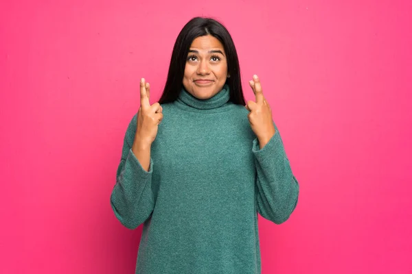 Young Colombian girl with green sweater with fingers crossing and wishing the best